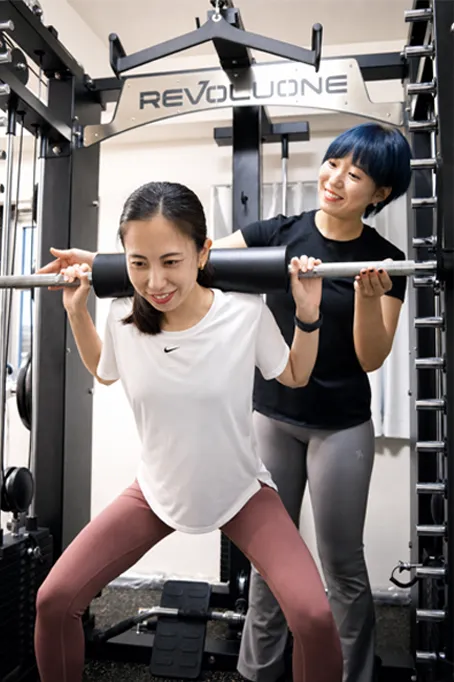 トレーナーのサポートを受けながらトレーニングする女性